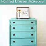 Teal chalk-painted dresser with dark knobs, decor, and framed art on top, against a white wall.