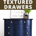 Dark blue dresser with gold knobs, textured drawer fronts, and a plant and sign on top against a white wall.