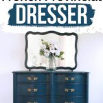 A blue French provincial dresser with gold handles, a mirror, and a vase of white flowers on top.