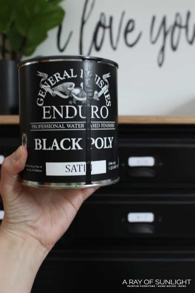 Holding General Finishes Black Poly in front of black painted dresser