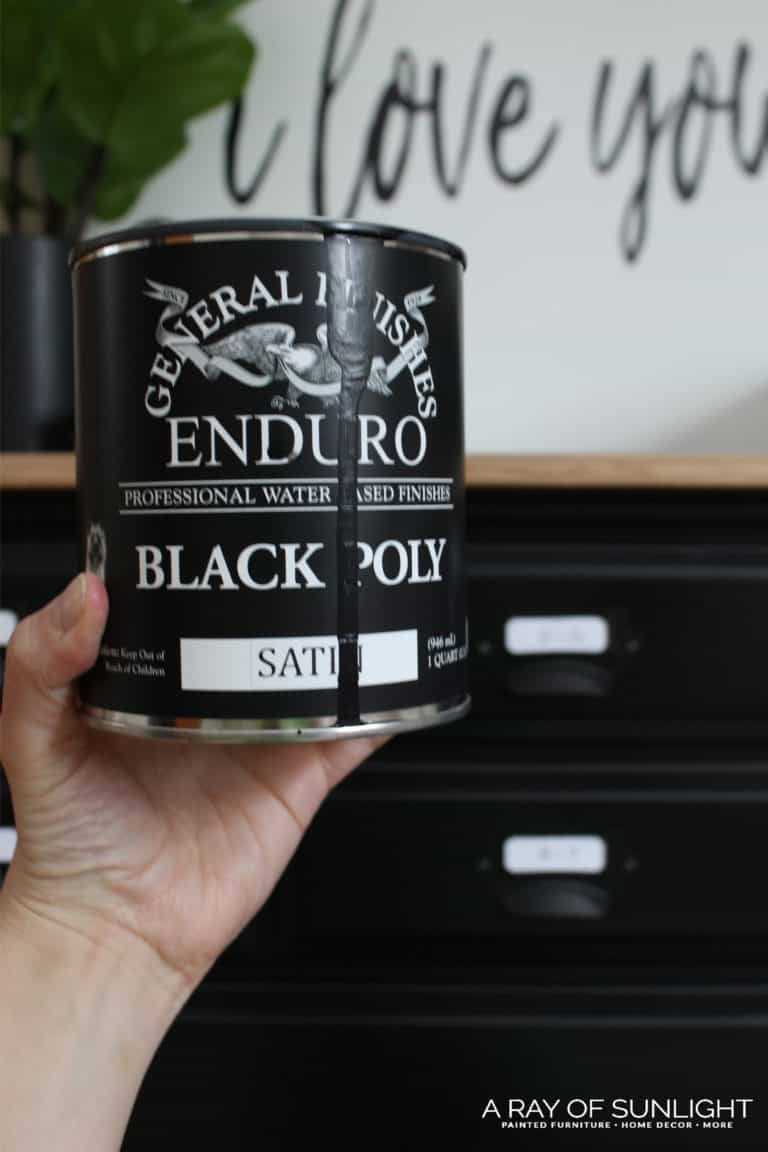 Holding General Finishes Enduro Pigmented Poly in Black in front of black painted dresser