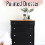 A black painted dresser with white knobs, decor on top, and text Black Milk Painted Dresser above it.