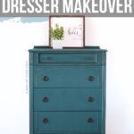 Teal painted vintage dresser with black knobs, decorated with a framed sign and a small potted plant on top.