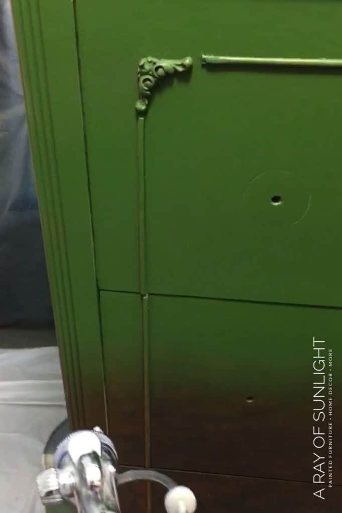 spraying emerald green milk paint onto the dresser