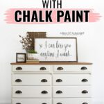 White dresser with dark handles, decor and a framed quote on top, with text about spray painting with chalk paint.