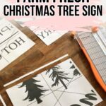 Printed sign pieces and a paper cutter on a wooden table for making a DIY Christmas tree sign.