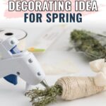 A glue gun attaching twine to dried flowers with spring crafting supplies in the background.