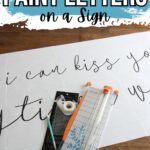 Paper with cursive letters, a paper cutter, pencil, and tape; text reads How to Paint Letters on a Sign.