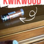 Hand holding a piece of KwikWood epoxy, with a KwikWood tube on a wooden dresser in the background.