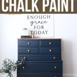 A navy blue dresser with gold knobs sits beneath a wall sign that reads Enough grace for today.