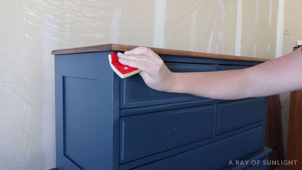 Sanding by hand between coats of polyurethane on blue painted furniture