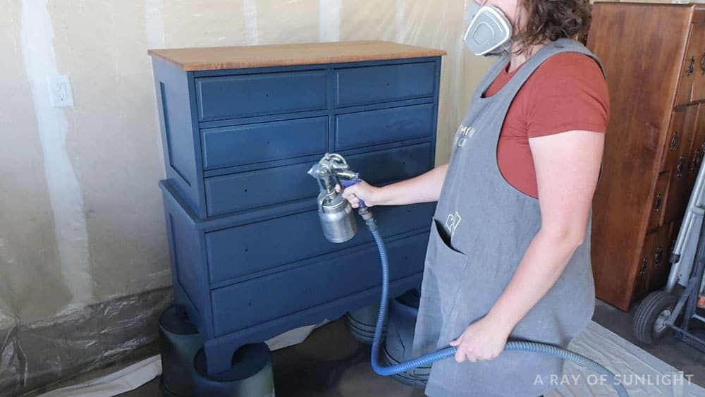 Spraying polyurethane on blue painted dresser