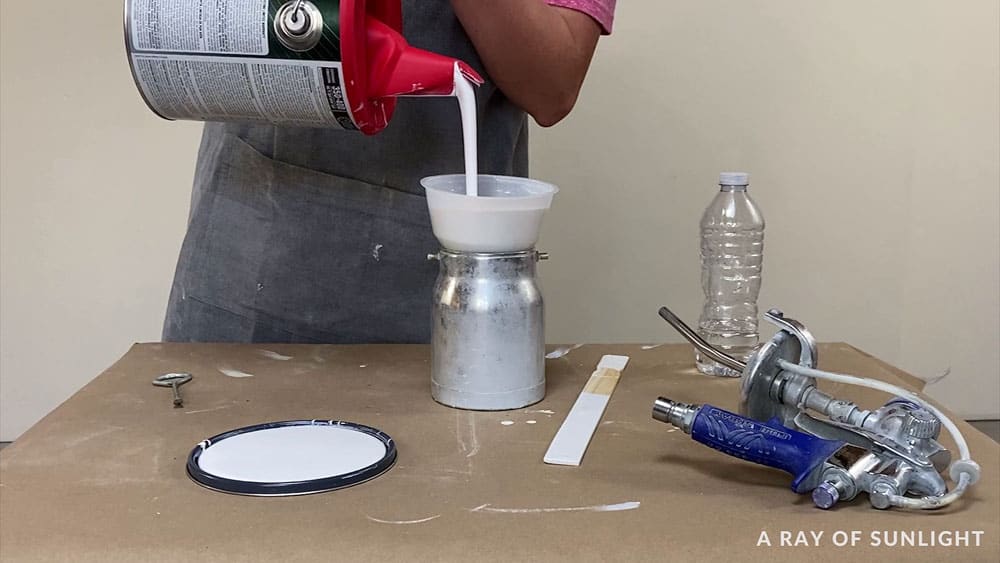 pouring alkyd paint into a filter and into the sprayer's container