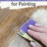 Hand sanding wood surface with purple sandpaper; text says “How to Prepare Furniture for Painting.”.