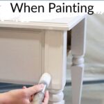 A hand painting a wooden table white with text: How to Hide Wood Grain When Painting.