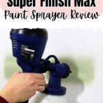 Hand using a HomeRight Super Finish Max paint sprayer to spray green paint on a white wall.