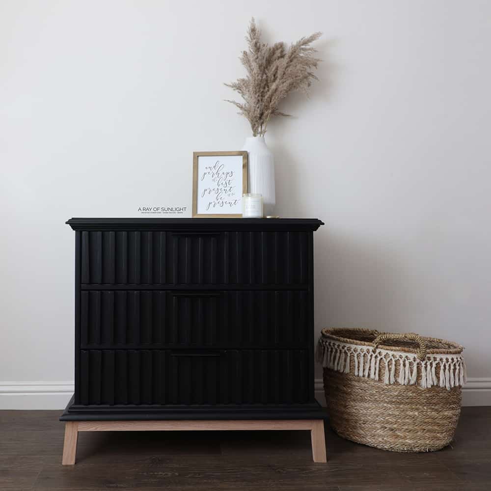 full view of the black painted dresser with slatted wood drawers and a natural basket next to it