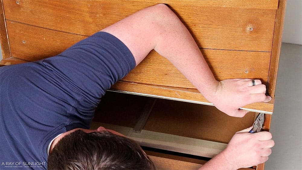 Removing a piece of metal trim from the front of a dresser.
