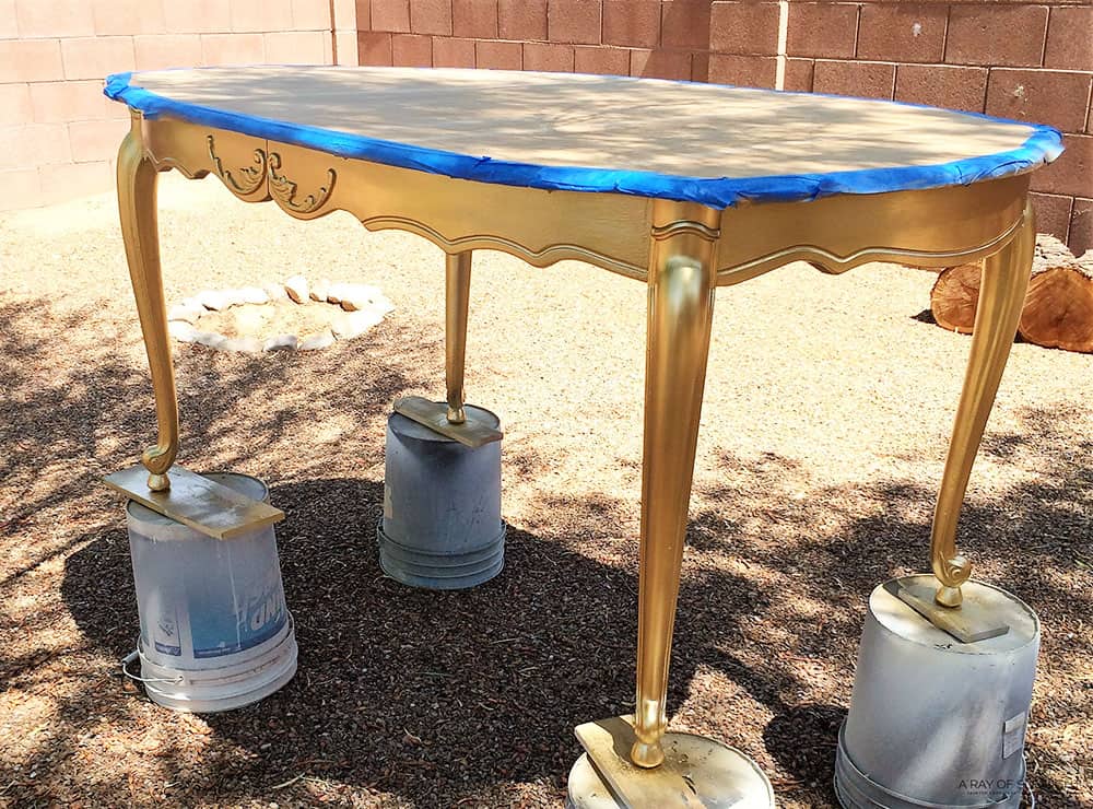 dining table after being spray painted with gold spray paint - in backyard, on 5 gallon buckets