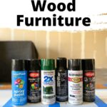 Six cans of spray paint are lined up on a table, labeled as the best spray paint for wood furniture.