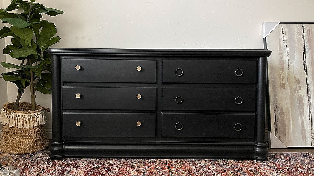 Black painted dresser with gold knobs on one side and black drawer pulls on the other side.