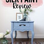 Blue side table with flowers and decor on top, against a white wall with Dixie Belle Silk Paint Review text.