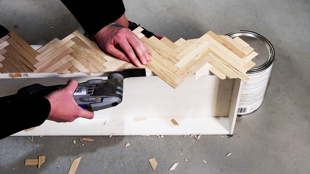 Using a multi-tool to cut overhanging popsicle sticks off the drawer front.