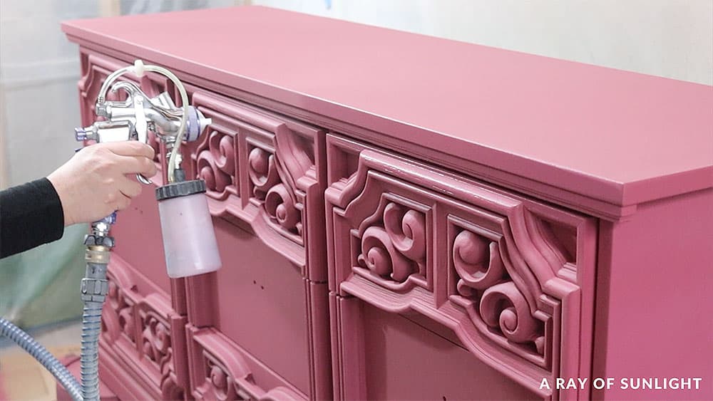 Spraying a coat of polyurethane top coat on a pink painted dresser