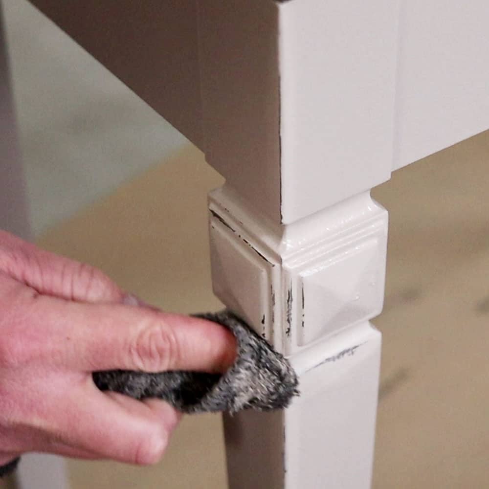 using a wet rag to wipe away wet paint on edges of furniture to create distressing
