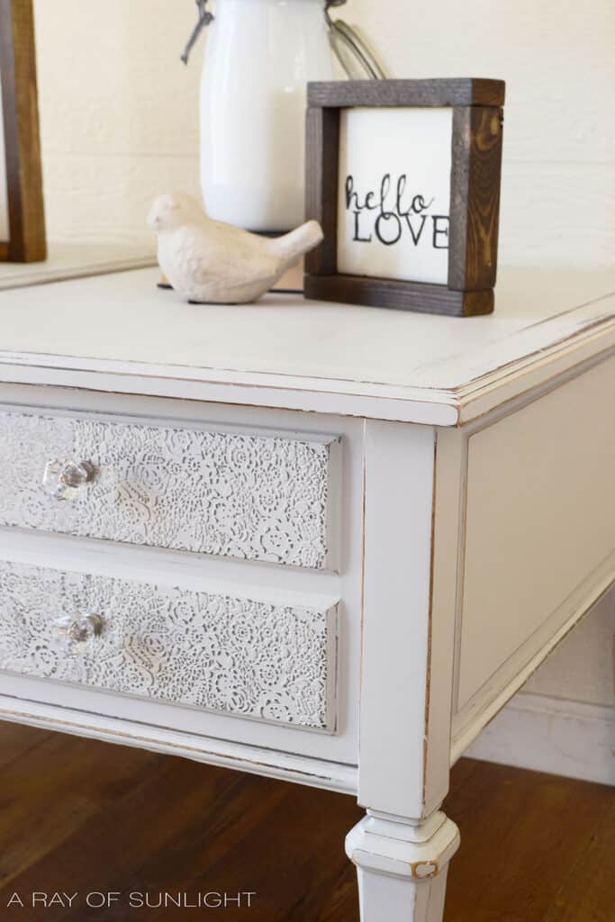 close up of light gray painted end table with raised stenciling on the drawers for a shabby chic look