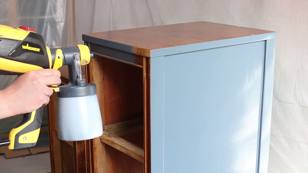 Spraying blue chalk paint onto nightstands with a paint sprayer.