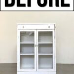 A white cabinet with glass doors sits below a large sign that says BEFORE in bold black letters.
