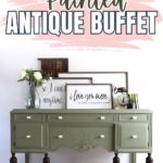Olive green painted antique buffet with dark legs, decor items, and framed art on top against a white wall.