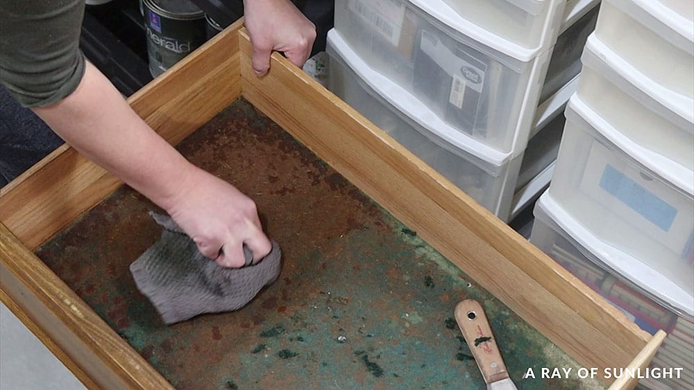 Using a damp rag and razor blade to remove old felt in the bottom of a drawer.