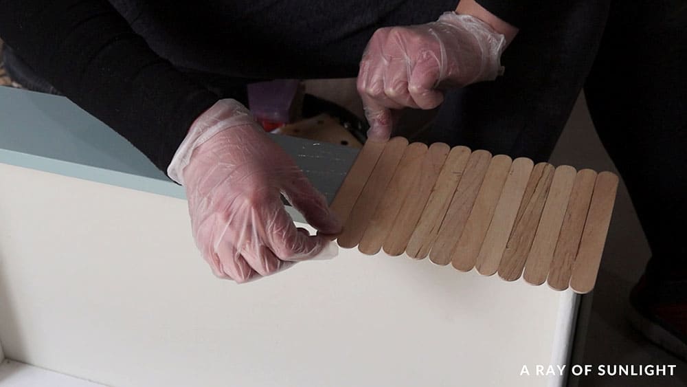 Gluing popsicle sticks to the drawer fronts to create a wood look.
