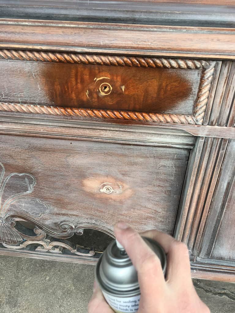spraying clear shellac onto the antique buffet's surface