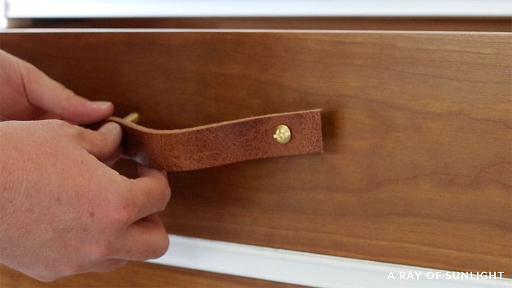 Attaching leather pull hardware to the drawer fronts.