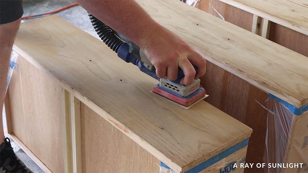 Using a SurfPrep sander to sand the remaining finish off the drawer fronts