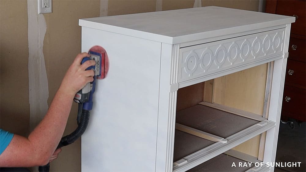 Using a SurfPrep sander to lightly sand the primer before painting the dresser.