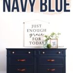 Navy blue dresser with copper handles, plant, and framed quote sign above against white wall.