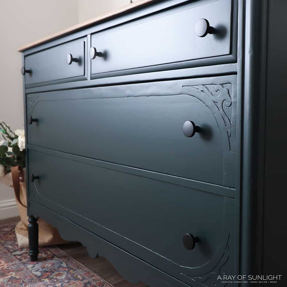 Green painted dresser with black knobs from a close side view.