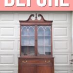 A wooden china cabinet stands in front of a garage door with BEFORE in large letters above it.
