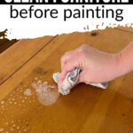Hand with a cloth wiping soapy water on a wooden table, text says How to Clean Furniture before painting.