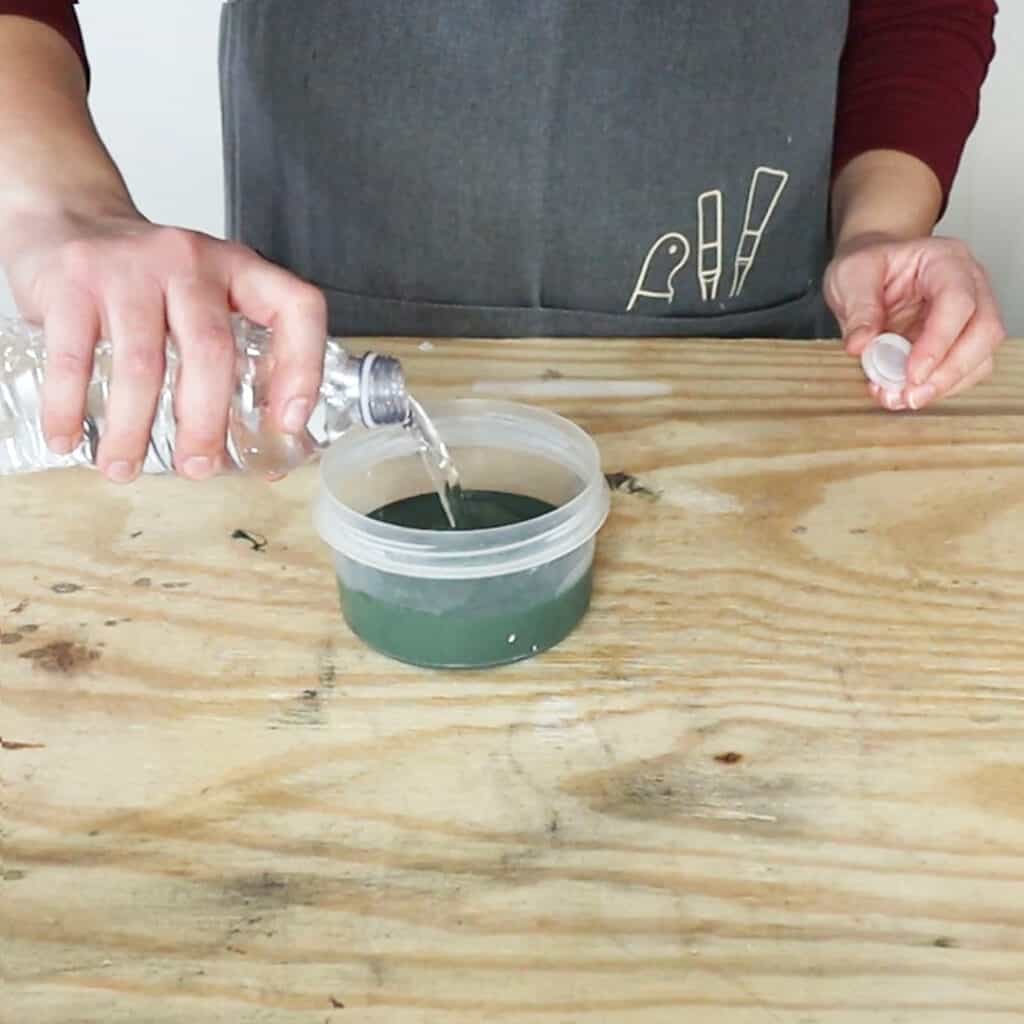 pouring water into a bowl of chalk paint to thin the paint