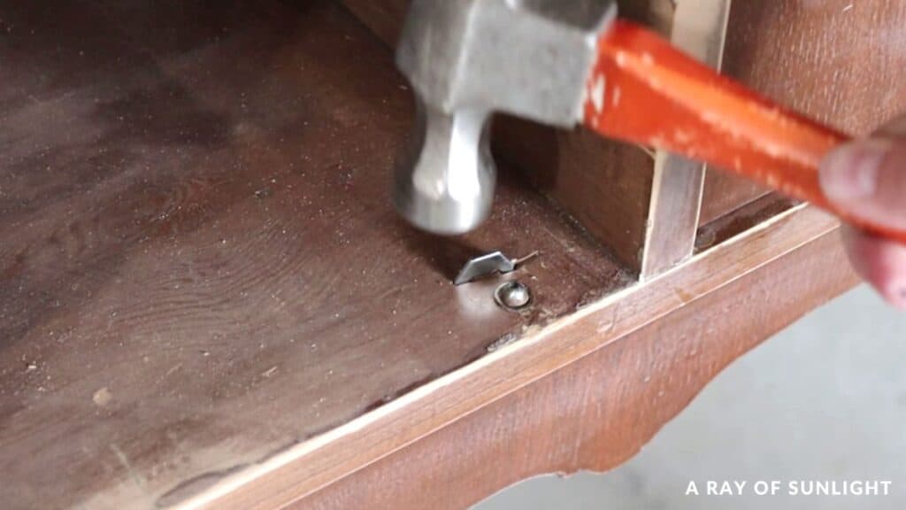 Using a hammer to install metal door stoppers in the cabinets on a buffet.
