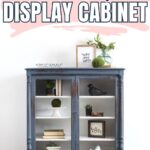 Blue painted display cabinet with glass doors, decorated with books, plants, and small ornaments.