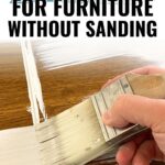 A hand painting white paint on brown wood furniture with text: Best Paint for Furniture Without Sanding.