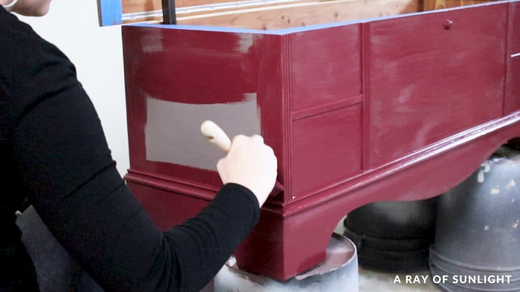 brushing first coat of red enamel paint onto cedar chest