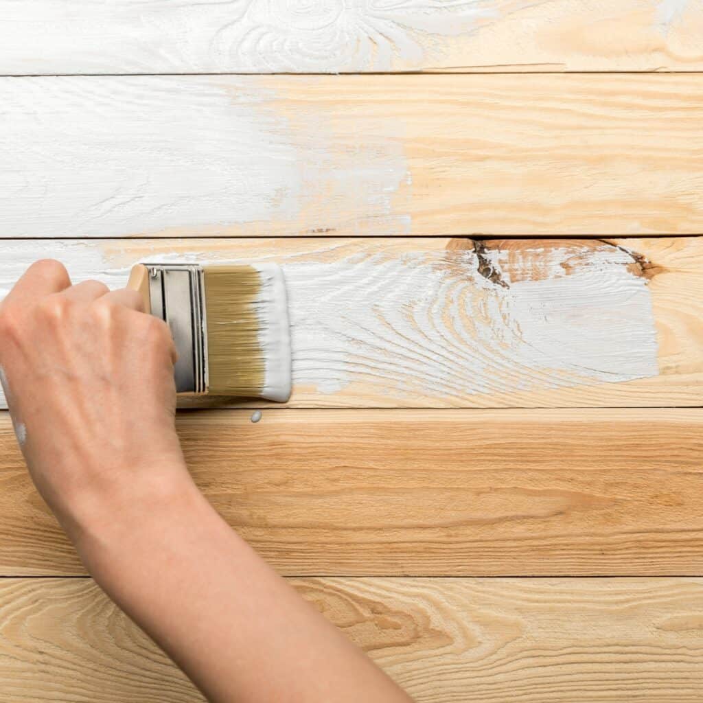 brushing gray paint on wood surface with a wood knot