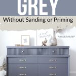 A grey painted dresser with gold handles sits against a wall, decorated with art and accessories.